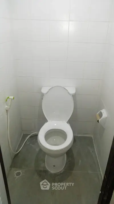 Compact bathroom with white tiled walls and basic toilet setup.