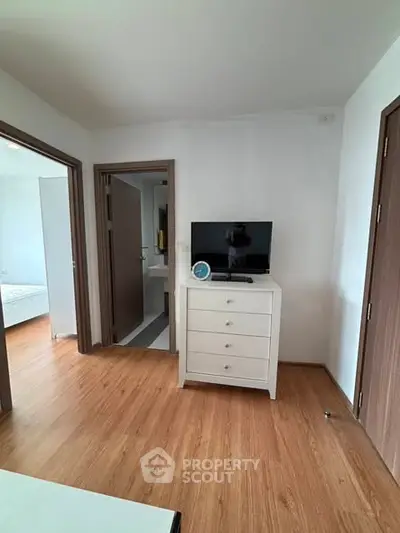 Modern bedroom with wooden flooring and white dresser, featuring a flat-screen TV and open doorways.