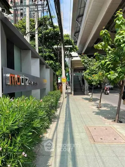 Modern urban sidewalk near residential building with lush greenery and city infrastructure.