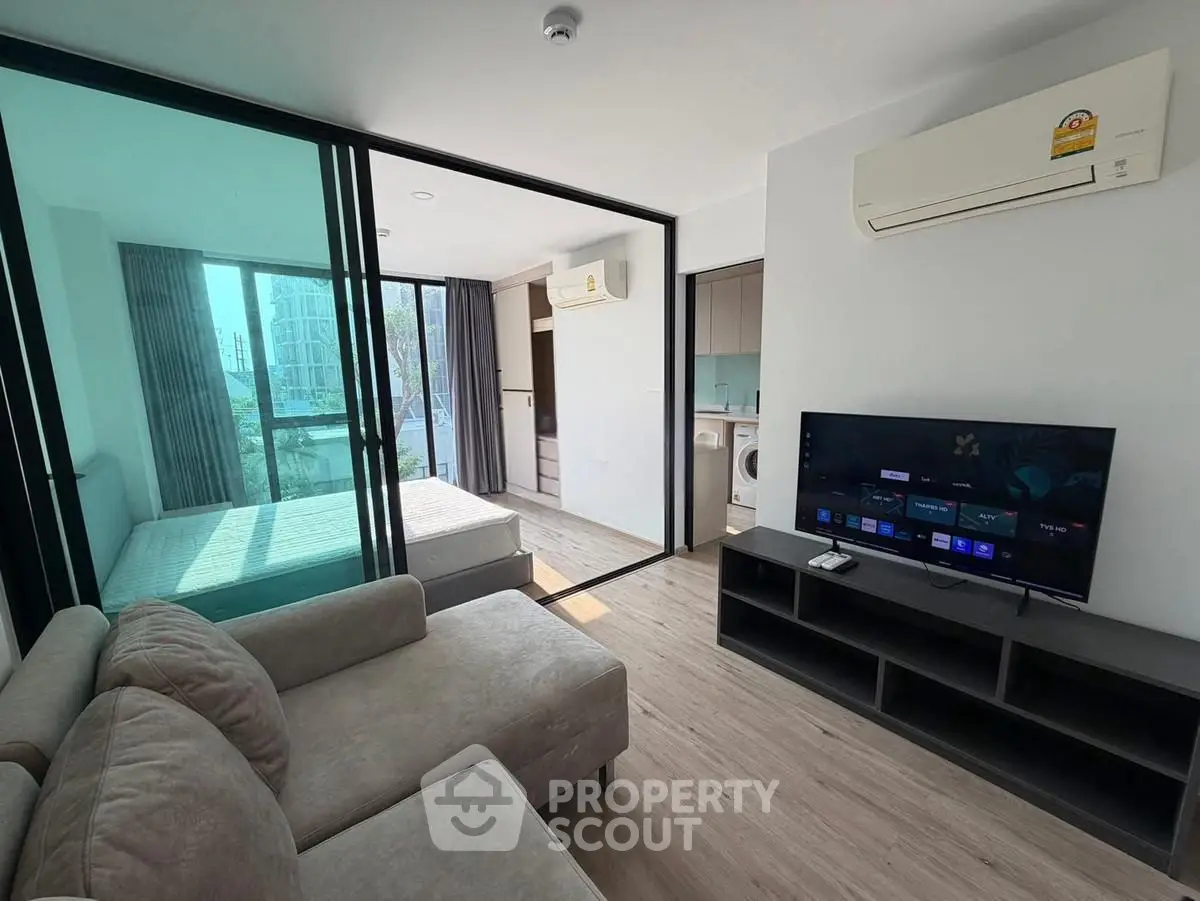 Modern apartment interior with open layout, featuring a cozy living room and adjacent bedroom with natural light.