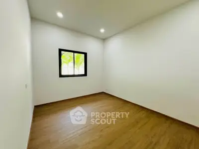 Spacious empty room with wooden flooring and a window offering natural light.