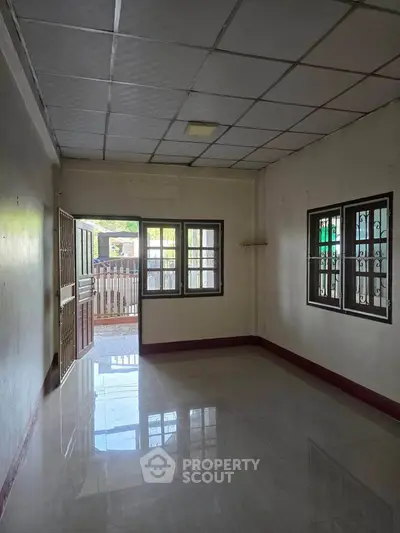 Spacious empty room with tiled flooring and natural light from windows, ideal for customization.