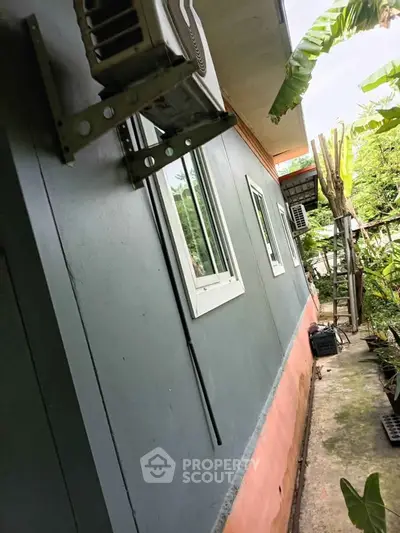 Exterior view of a residential building with air conditioning units and lush greenery.