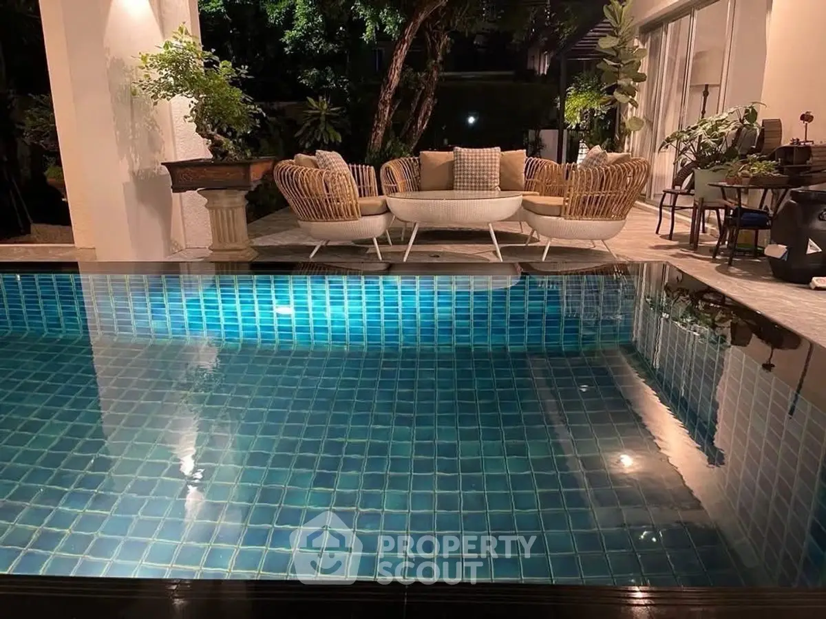 Luxurious poolside patio with elegant seating and lush greenery at night.
