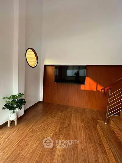 Modern living room with wooden flooring, wall-mounted TV, and stylish round window.