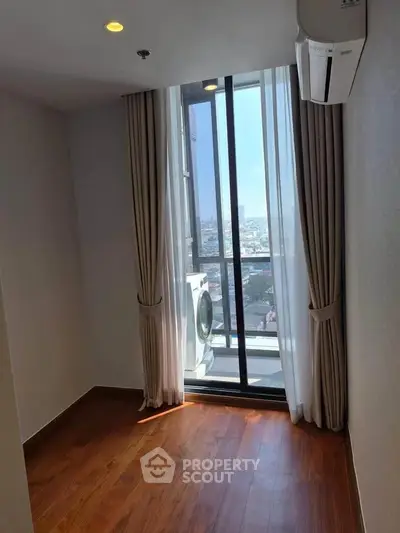 Bright room with wooden flooring and large window offering city view, featuring a washing machine.