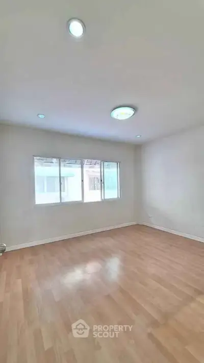 Spacious empty room with wooden flooring and large window, ideal for customization.
