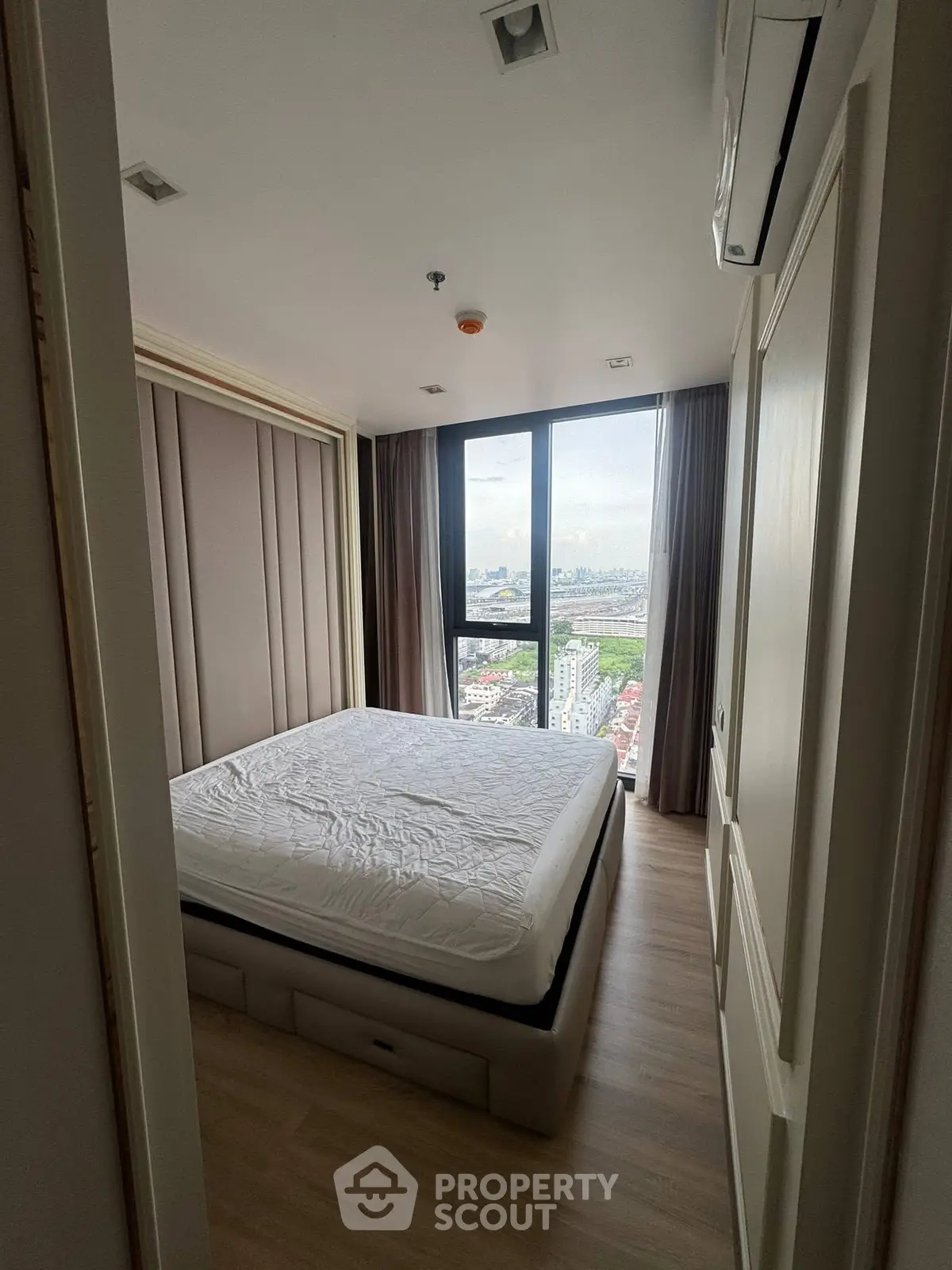 Modern bedroom with large window offering stunning city view in high-rise apartment.