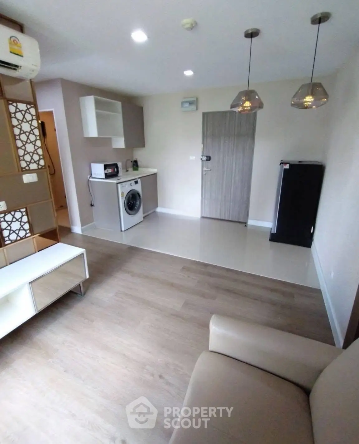 Modern living room with integrated kitchen featuring washing machine and stylish lighting.