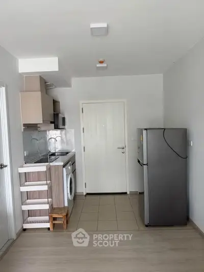 Modern compact kitchen with washing machine and fridge in a sleek apartment.
