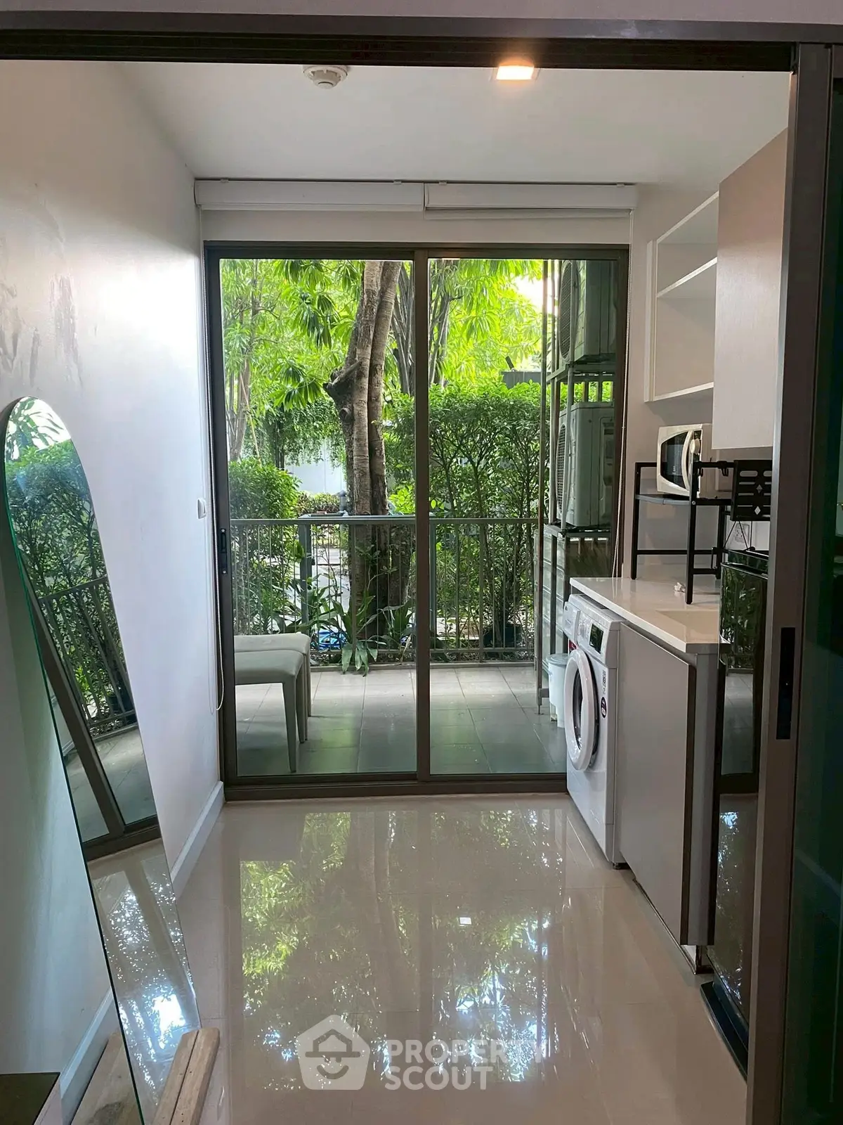 Modern condo with balcony, washing machine, and lush garden view.