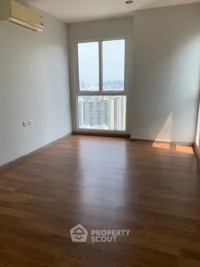 Spacious empty room with wooden flooring and city view from window
