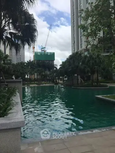 Luxurious residential pool area with lush greenery and modern high-rise buildings.