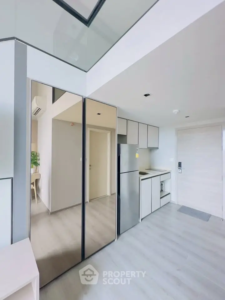 Modern apartment interior with sleek kitchen and mirrored storage, featuring minimalist design and bright lighting.
