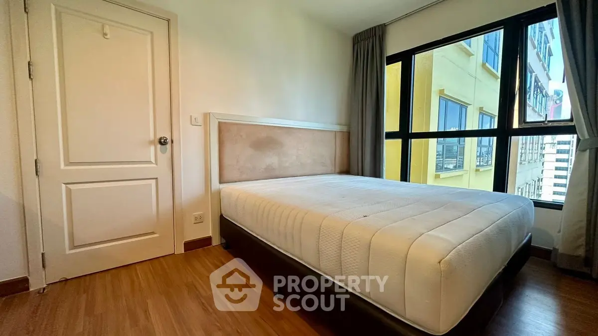 Cozy bedroom with large window and wooden flooring in modern apartment