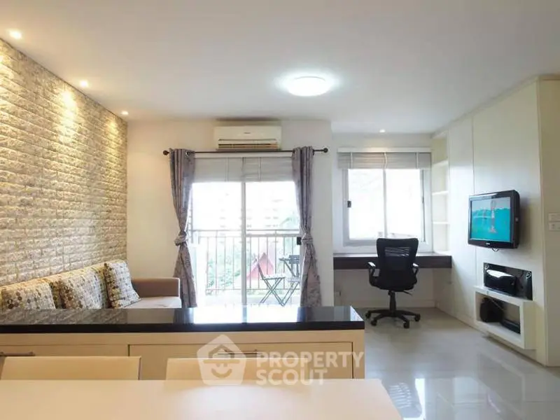 Modern living room with balcony and workspace, featuring stylish decor and ample natural light.
