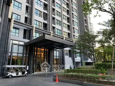 Modern high-rise building entrance with lush landscaping and sleek design.