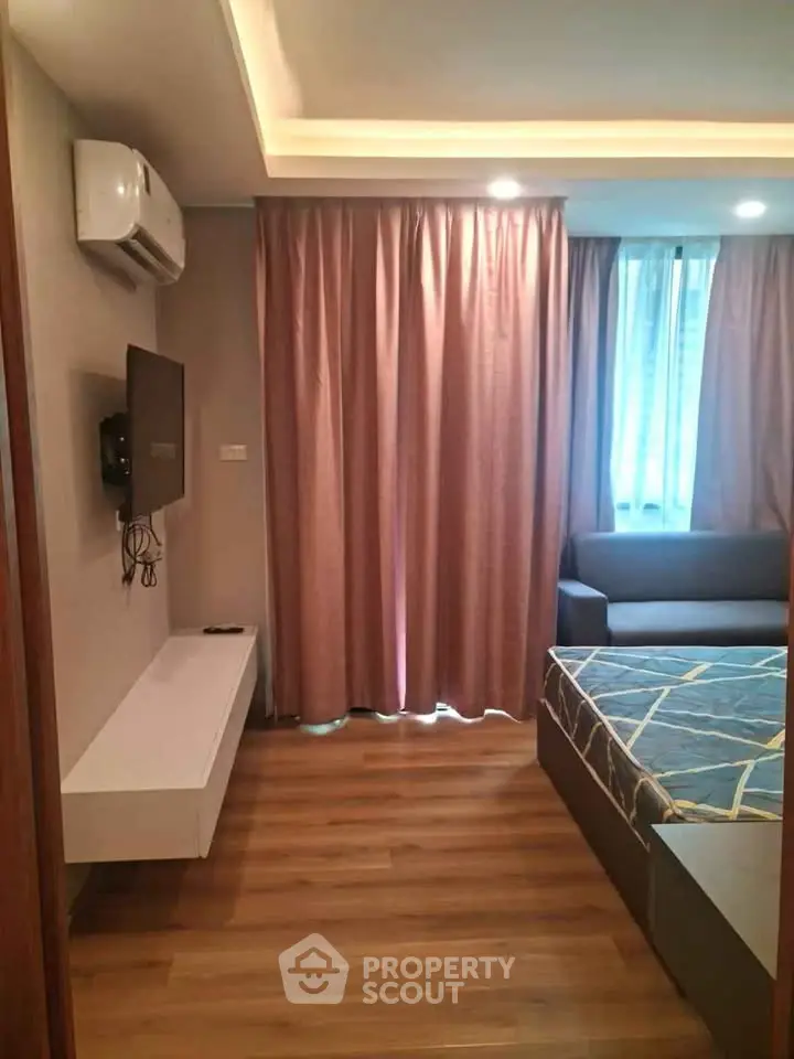 Modern bedroom with wooden flooring, wall-mounted TV, and elegant curtains.