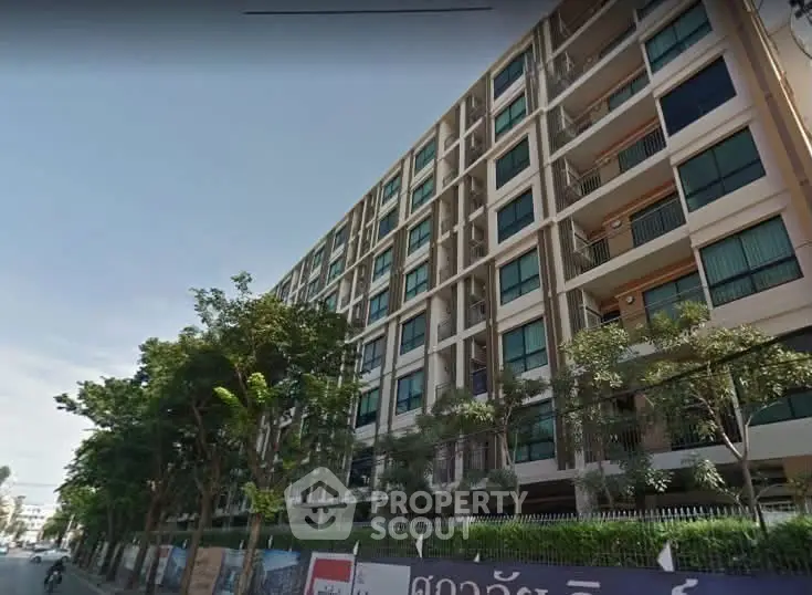 Modern multi-story apartment building with lush greenery and street view.