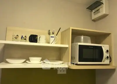 Modern kitchen with microwave and open shelving displaying dishes and mugs.