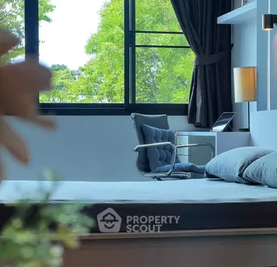 Modern bedroom with large window and stylish chair, offering a serene view of lush greenery.