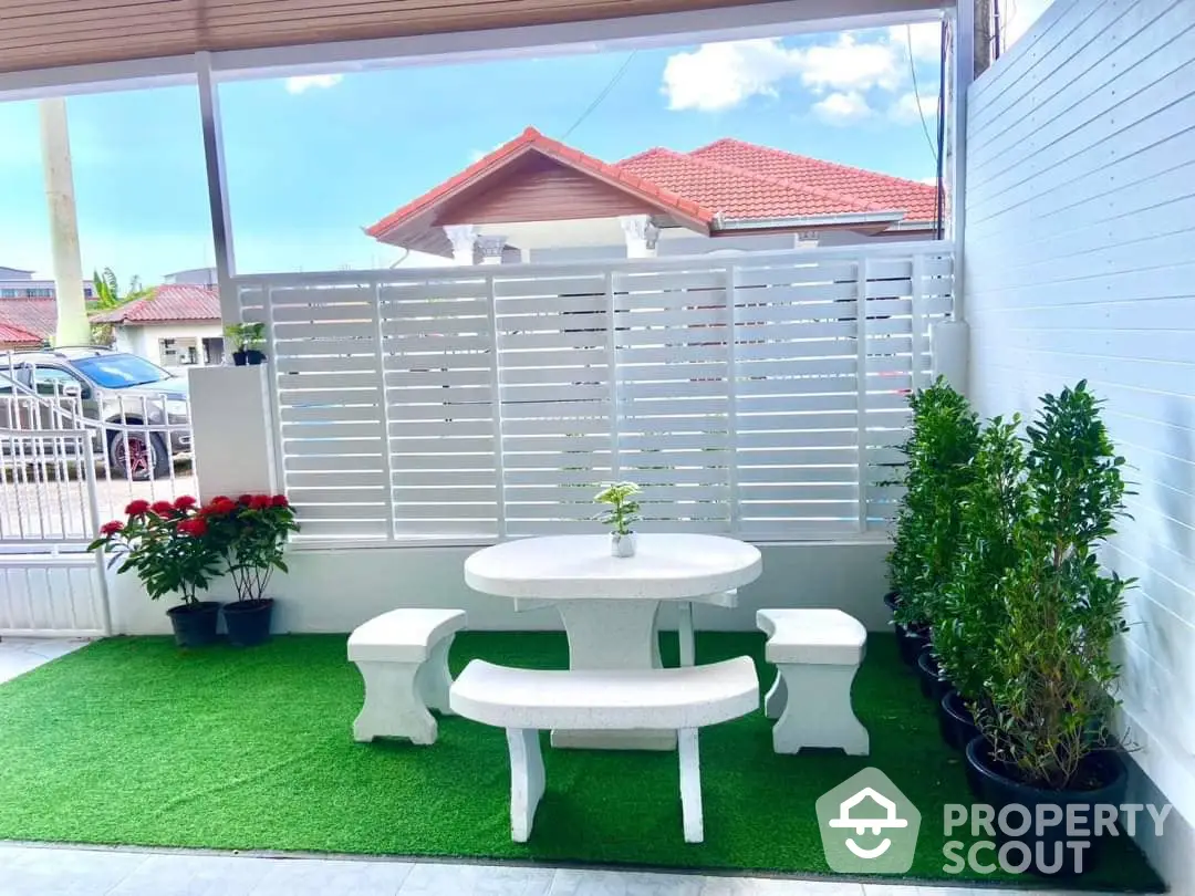 Charming outdoor patio space with artificial grass, a white round table with seating, and vibrant potted plants enhancing the cozy ambiance.