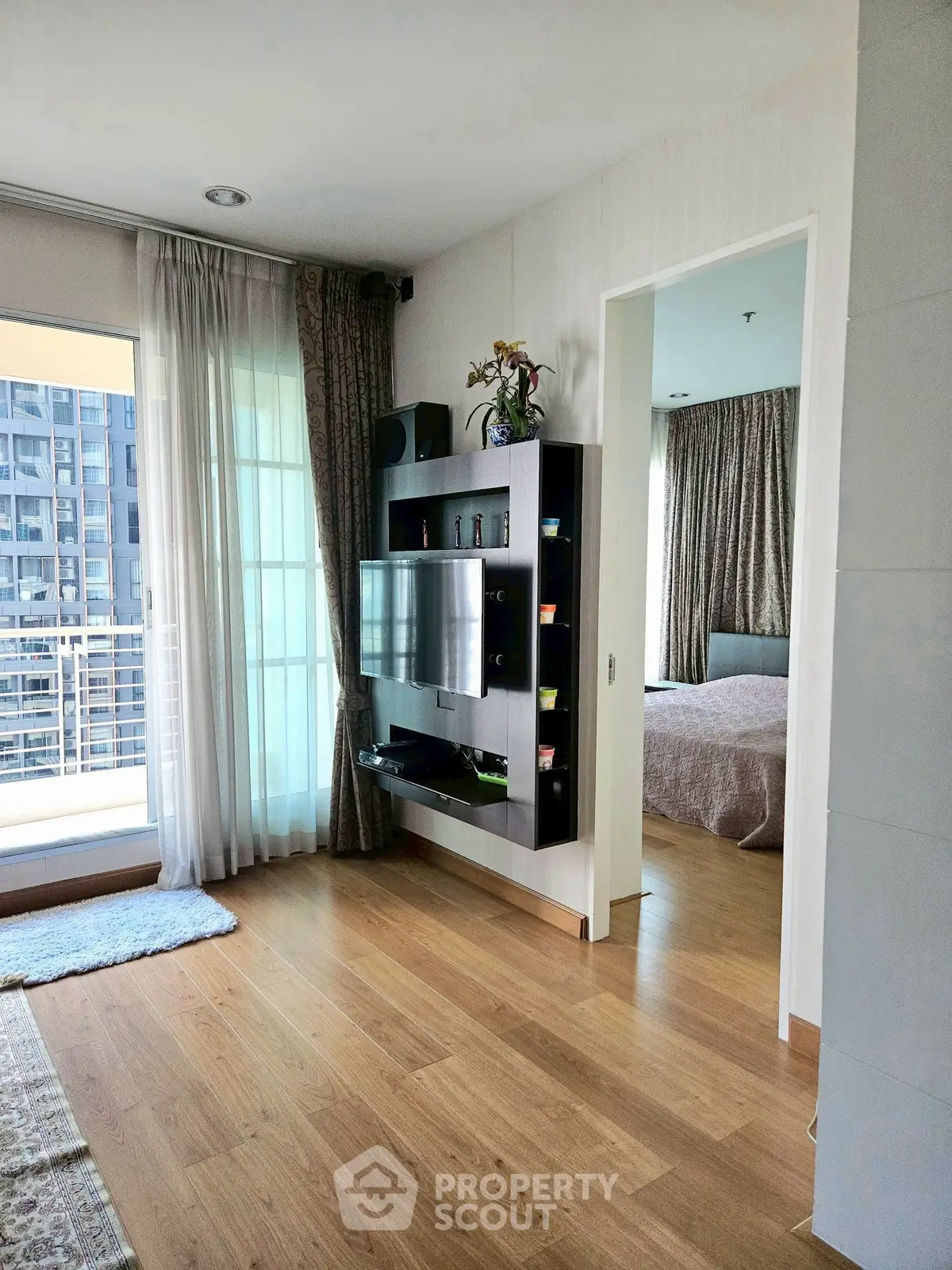 Modern apartment interior with open living area and bedroom, featuring wooden flooring and large windows.