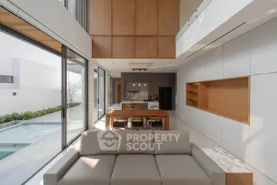 Luxurious modern living room with open kitchen and pool view, featuring high ceilings and elegant design.