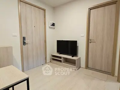 Modern minimalist living room with light wood flooring and doors, featuring a sleek TV stand and flat-screen TV.