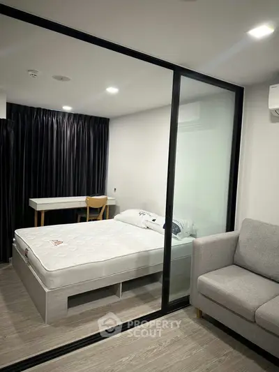 Modern bedroom with glass partition, cozy sofa, and study desk in a stylish apartment.