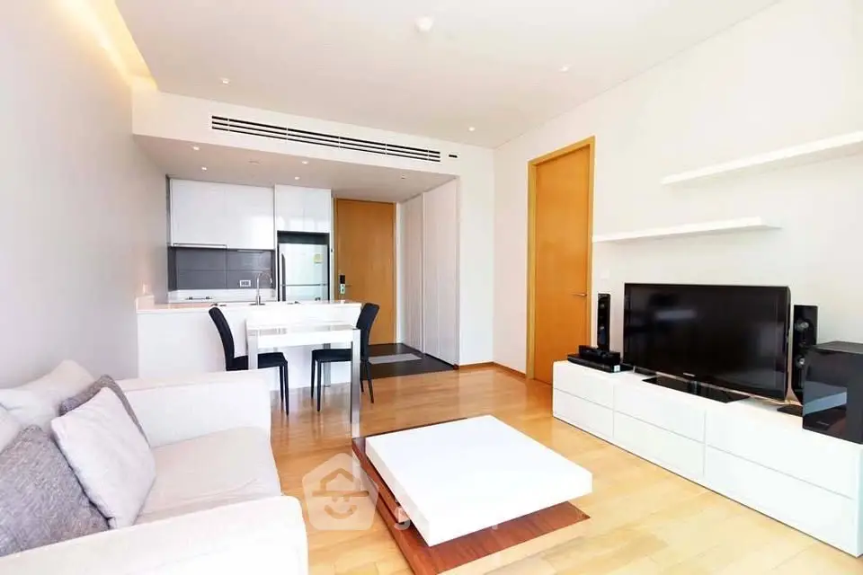 Modern living room with open kitchen, sleek furniture, and wooden flooring in a bright apartment.