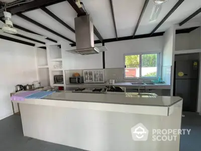 Spacious modern kitchen with large center island, gas stove, and sleek white cabinetry, set against exposed beams for a contemporary rustic charm.