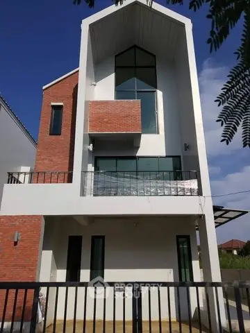 Modern three-story house with unique architecture and large windows, featuring a small balcony and brick accents.