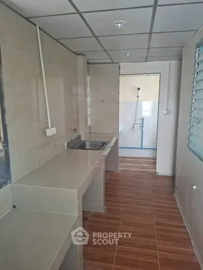 Modern kitchen with sleek countertops and tiled flooring, featuring a stainless steel sink and ample natural light.