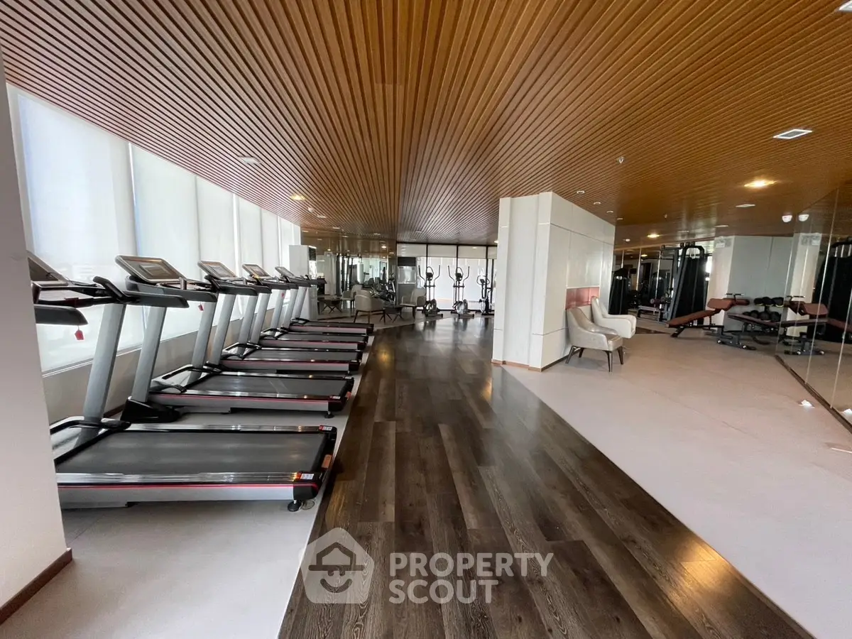 Luxurious gym with modern equipment and stylish wooden ceiling in upscale residential building.