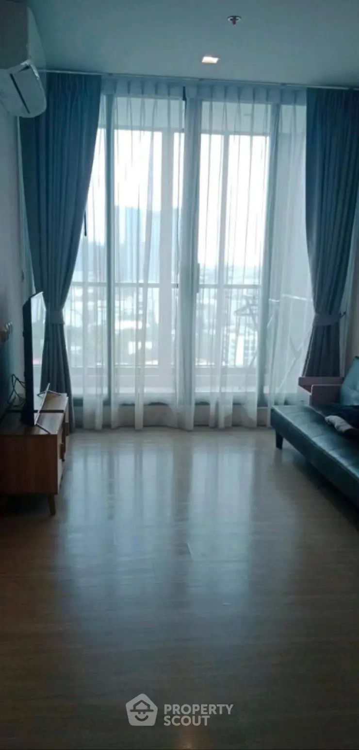 Spacious living room with large windows and modern furnishings in a high-rise apartment.