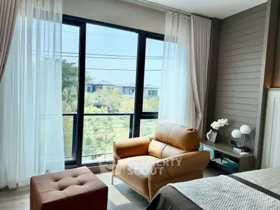 Bright bedroom with large windows and cozy seating area overlooking lush greenery.
