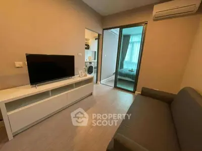 Modern living room with TV, sofa, and view into bedroom with washing machine.