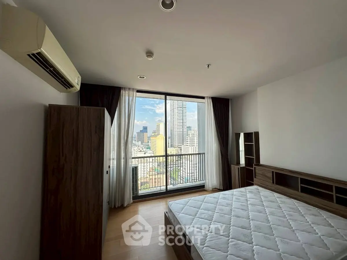 Spacious bedroom with city view and modern furnishings in high-rise apartment.