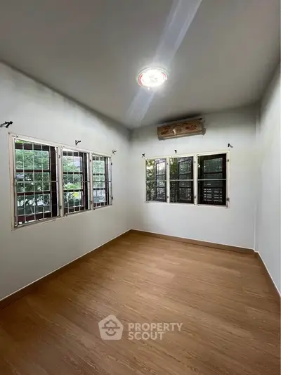Spacious room with wooden flooring and large windows offering natural light.