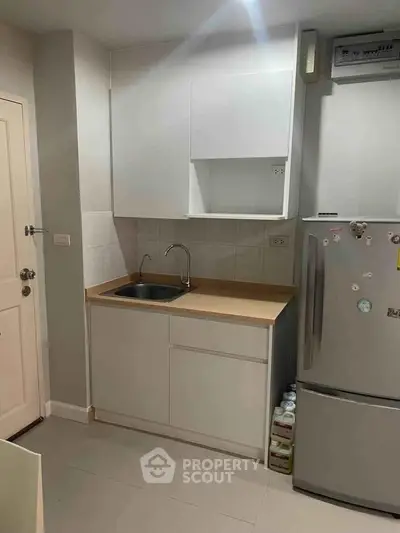 Compact kitchen with modern cabinetry and stainless steel fridge in cozy apartment.