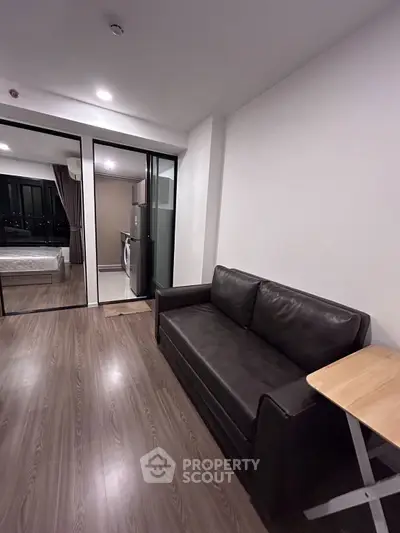 Modern apartment interior with sleek sofa and wooden flooring, featuring a view into a cozy bedroom.