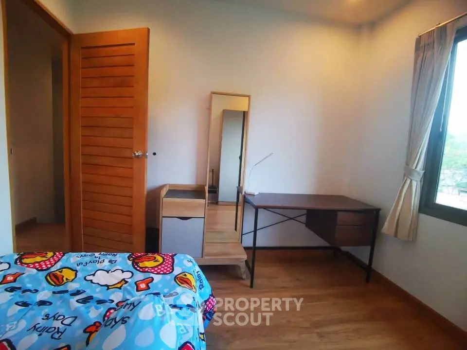 Cozy bedroom with wooden flooring, desk, and colorful bedding