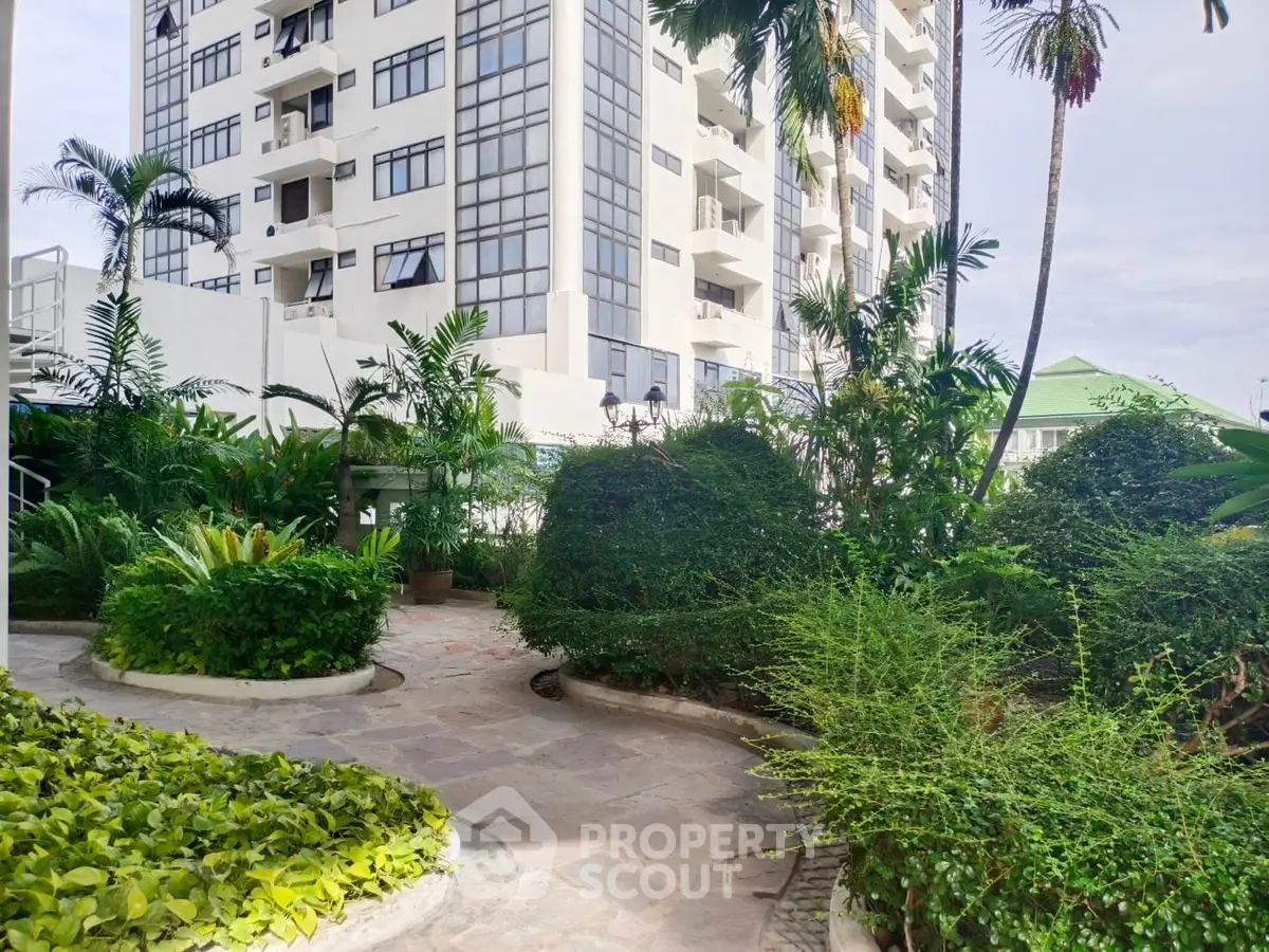 Luxurious high-rise building with lush garden and palm trees, perfect for serene urban living.