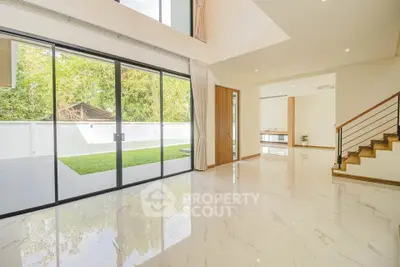 Spacious modern living room with large glass doors opening to a lush garden view.