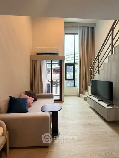 Modern living room with high ceiling and mezzanine, featuring stylish furniture and large windows for natural light.