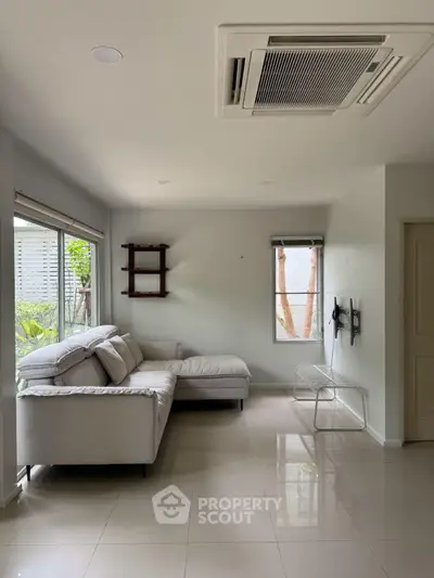 Spacious living room with modern sofa and large windows offering natural light and garden view.
