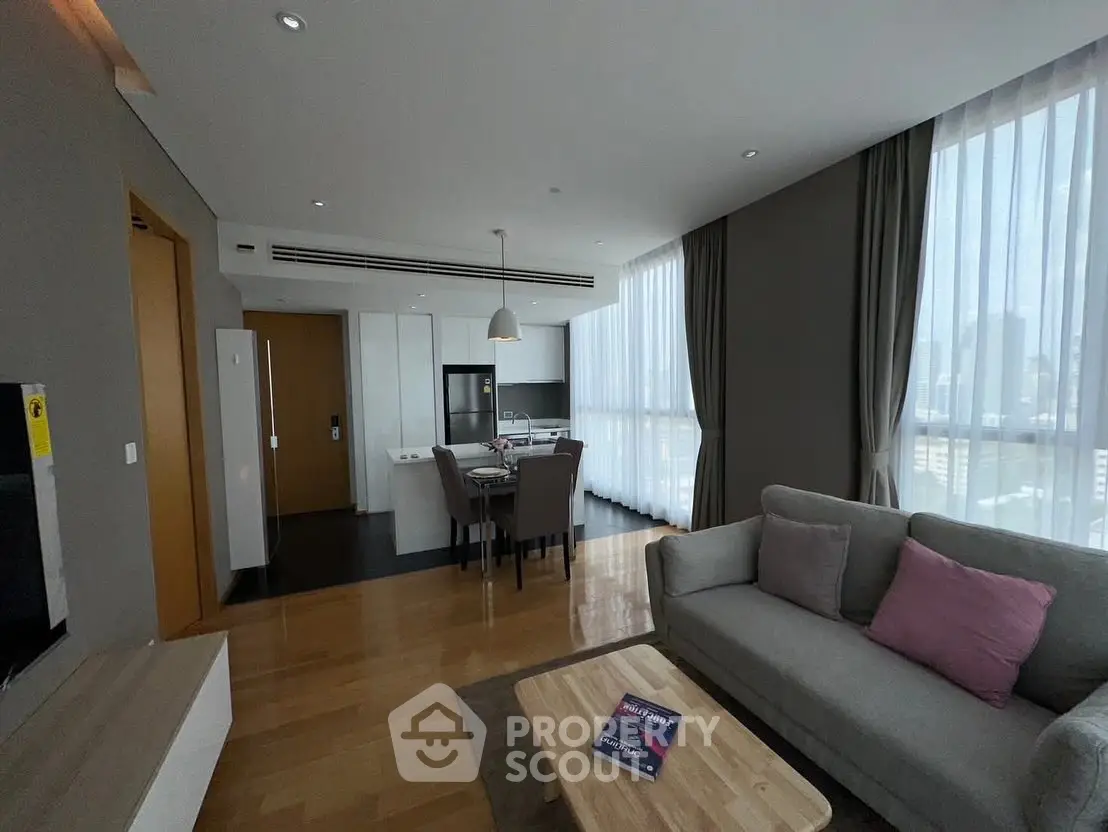 Modern open-plan living room with dining area and kitchen, featuring large windows and stylish decor.