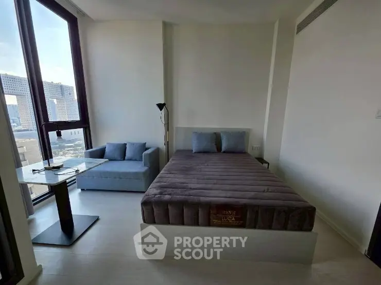 Modern bedroom with large windows and city view, featuring a cozy bed and stylish seating area.