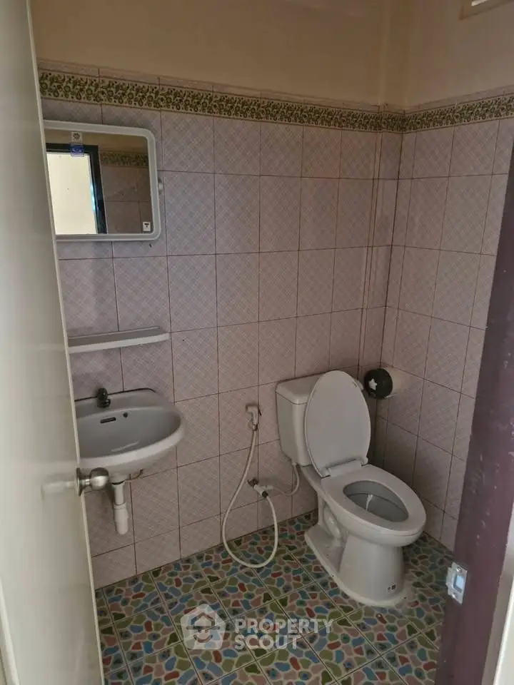 Compact bathroom with tiled walls and floor, featuring a toilet and sink.